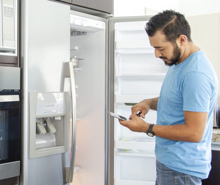 Homeowner looking in fridge while consulting phone