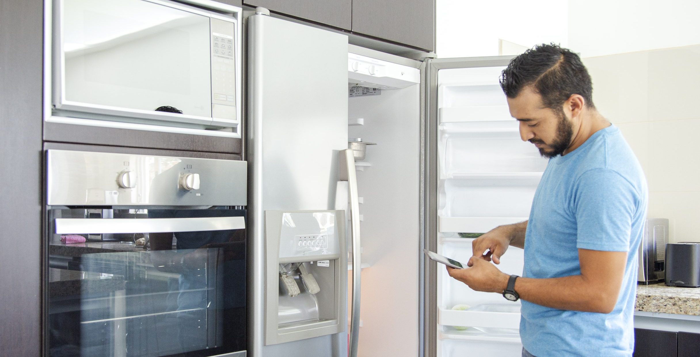 Homeowner looking inside fridge while consulting phone