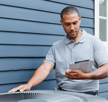 Contractor examining home HVAC unit outside and consulting tablet