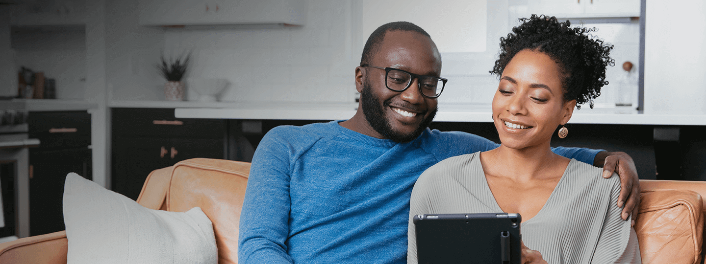 Couple sitting together on couch and smiling at tablet