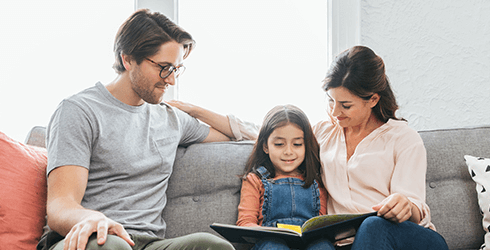 Couple sitting on couch with daughter, reading book together