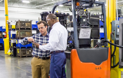 TVA employee and business worker in warehouse talking in front of a forklift