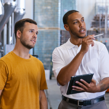 Contractor talking to worker, holding tablet and pointing with stylus