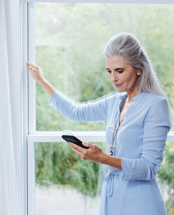 Woman examining window sealing while looking at phone