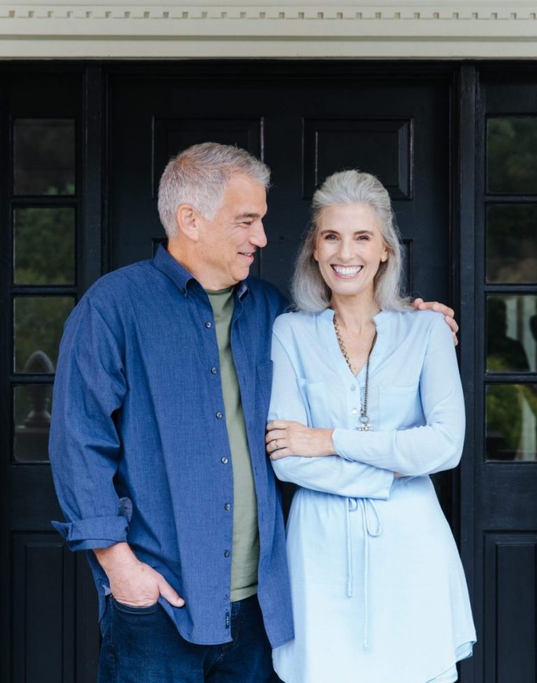 Older couple standing in front of house, smiling and hugging