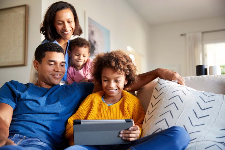 Family with two kids sitting on couch, smiling and looking at tablet
