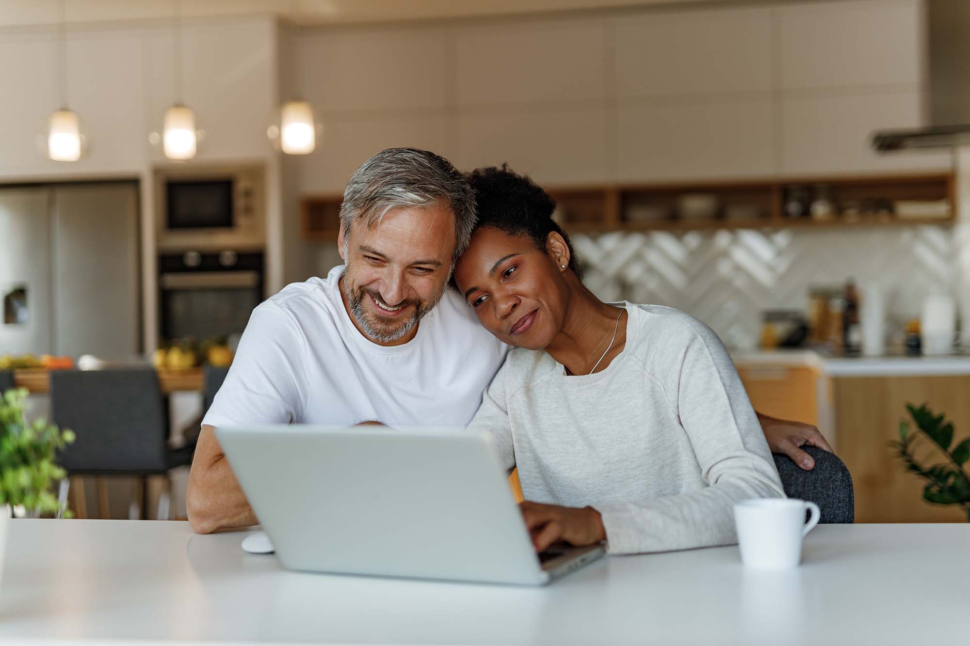 Couple in kitchen sitting together and looking at laptop