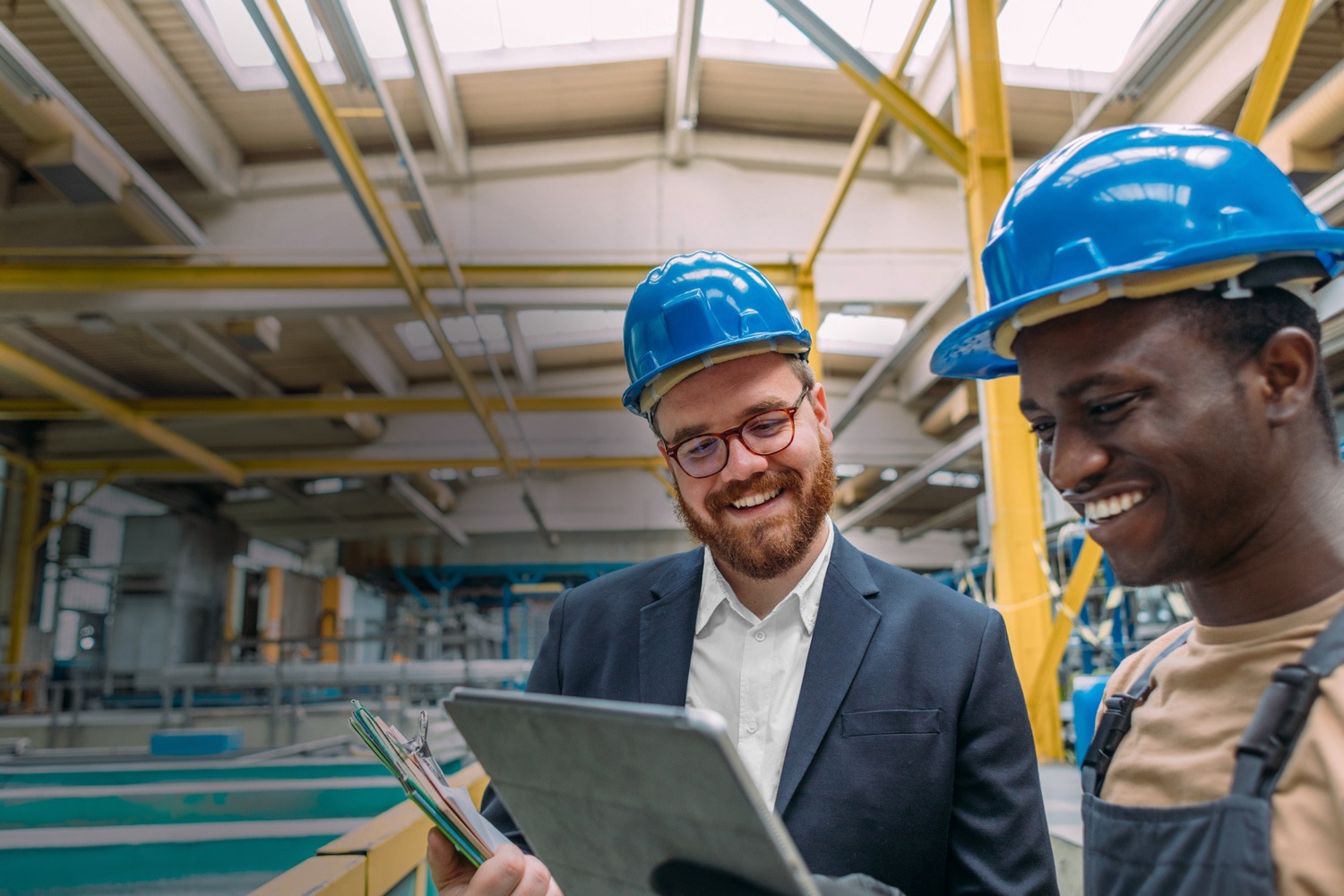 Two businessmen in hard hats talking in warehouse with tablet