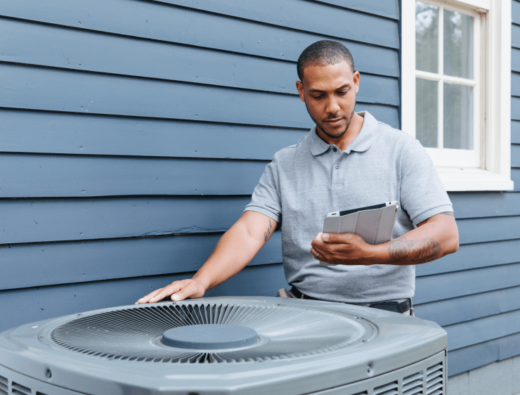 Contractor examining home HVAC unit while holding tablet