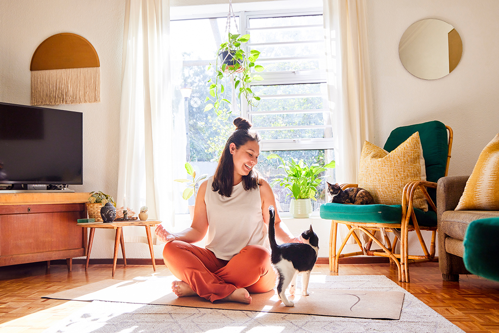 Woman doing yoga in her living room, interrupted by her cat