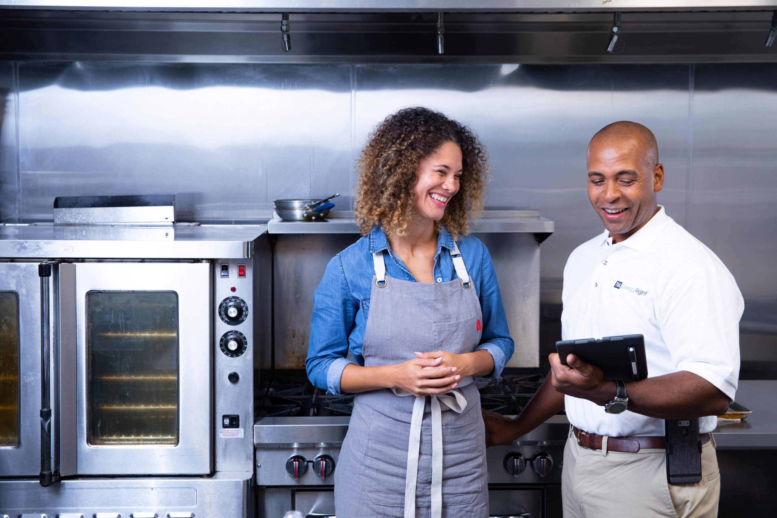 A woman looks at a tablet with an EnergyRight employee in an industrial kitchen
