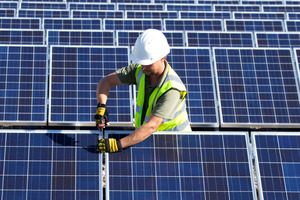 Person with light-colored skin wearing a safety vest and white hardhat installing a solar array.