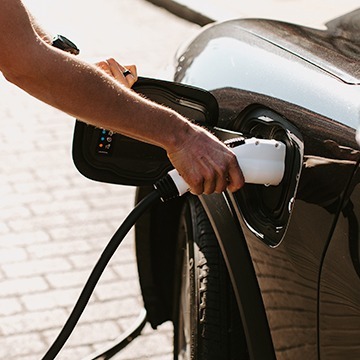 Close-up of person inserting a charging nozzle into an EV charging port.