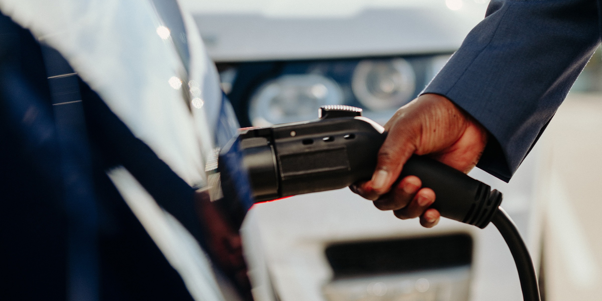 Close-up of a hand inserting a charger into an EV charging port.