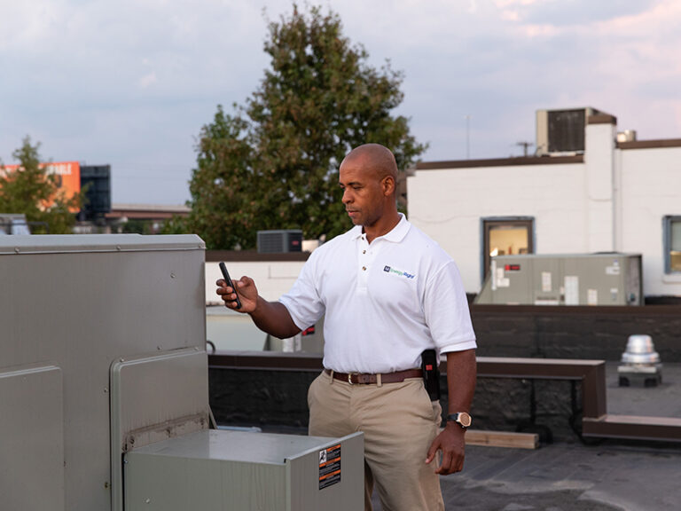 Man in white TVA EnergyRight polo shirt inspecting an HVAC unit.