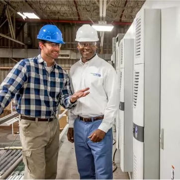 Two men in hard hats talking about energy efficiency in an industrial or commercial setting.