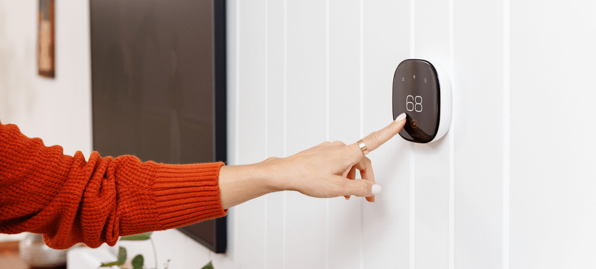 Woman's hand touching a smart thermostat.