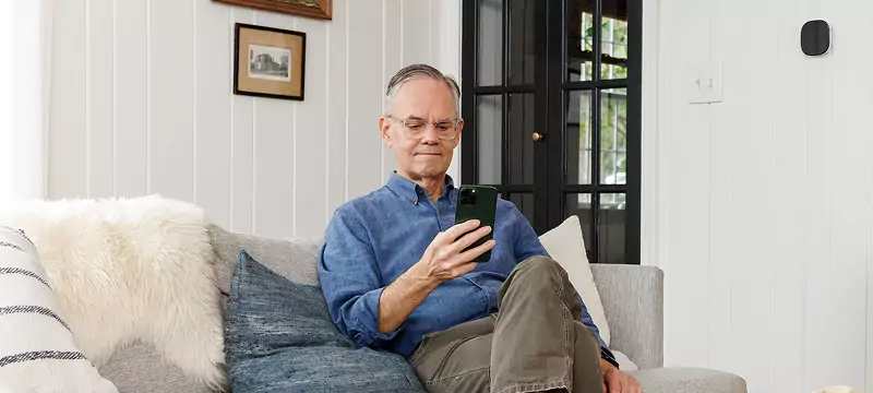 Late middle-aged man holding a cell phone. There's a smart thermostat on the wall.