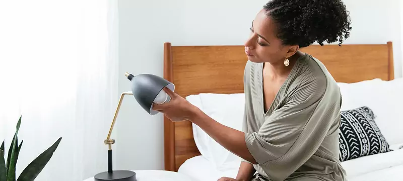 Young woman installing an LED light in her bedside reading lamp.