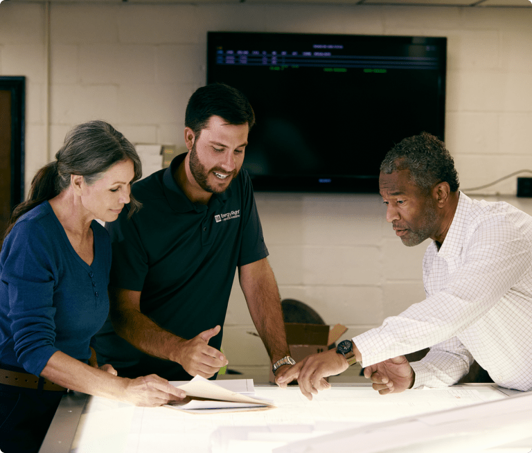 Three people review project plans at a table.