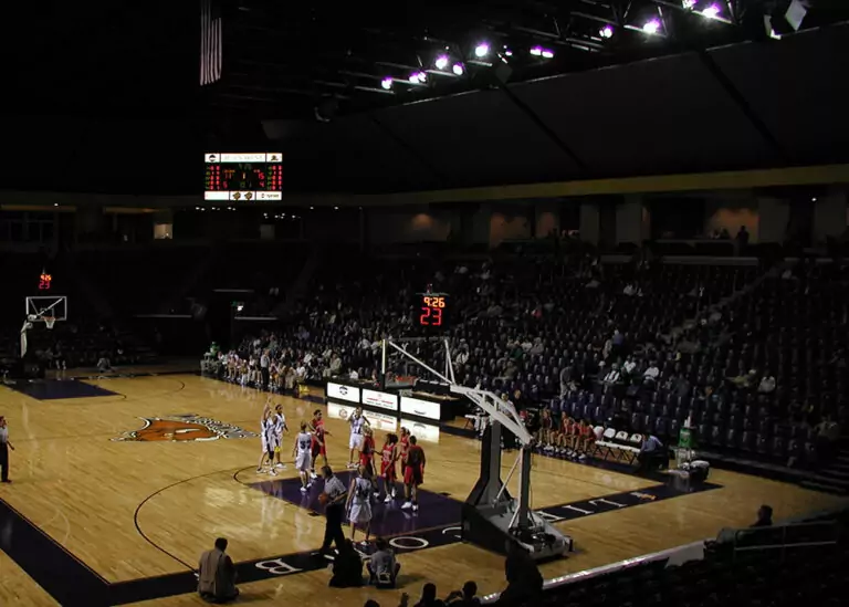 An indoor basketball game underway at Allen Arena, highlighting the high-intensity overhead stadium lighting system illuminating the court area and large-scale commercial facility infrastructure.