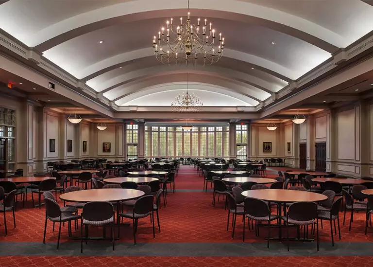 A large university dining facility at Memphis University School configured with rows of round tables, red carpeting, and an arched ceiling with elegant chandeliers.