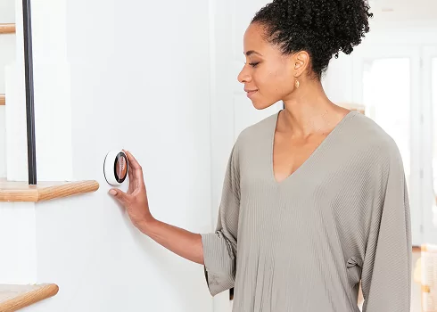 Woman adjusts a smart thermostat to easily control home climate and save energy.