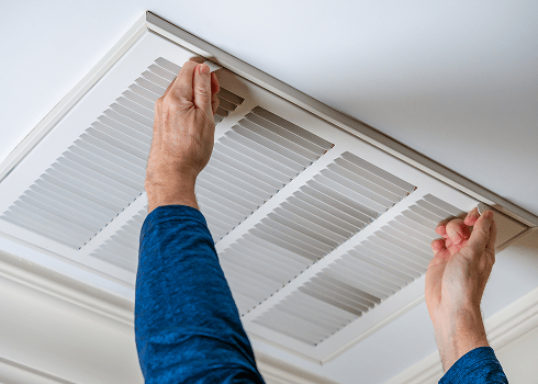 Hands adjusting a ceiling HVAC return vent for optimal system performance and energy savings.