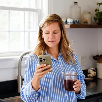 A TVA Energy Expert checks her phone in a kitchen, likely using an app to manage smart home energy or review usage.