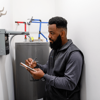 TVA Energy Expert taking notes while inspecting a water heater, assessing its energy efficiency.
