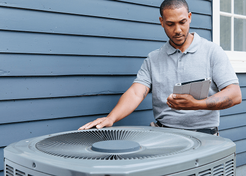 TVA Energy Expert inspects an outdoor energy-efficient heat pump unit, using a tablet for an energy assessment.