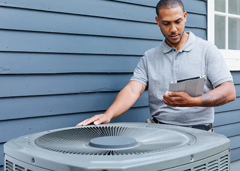 TVA Energy Expert inspects an outdoor energy-efficient heat pump unit, using a tablet for an energy assessment.