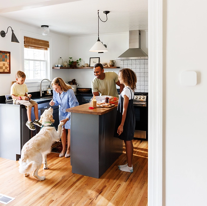 Family prepares breakfast in a bright, modern kitchen featuring a smart thermostat on the wall, promoting energy efficiency.