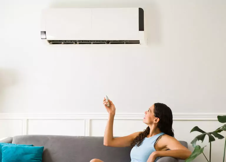 Resident adjusts a wall-mounted mini-split heat pump with a remote control for efficient home cooling and heating.