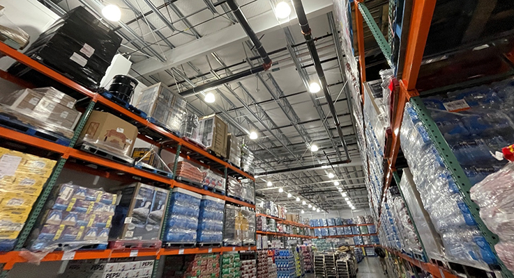 Vast warehouse with numerous bright overhead lights illuminating tall, stocked shelves, perfect for EnergyRight LED upgrades.