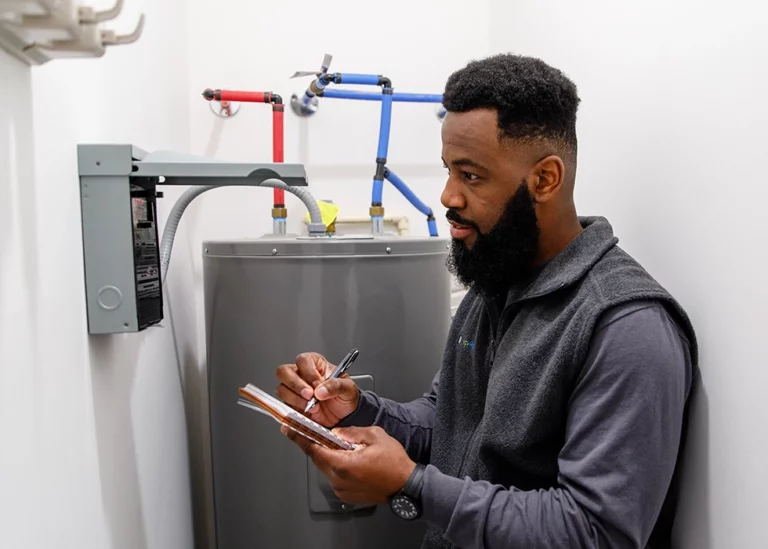 A TVA Energy Expert inspects an electric water heater, taking notes for energy efficiency upgrades.