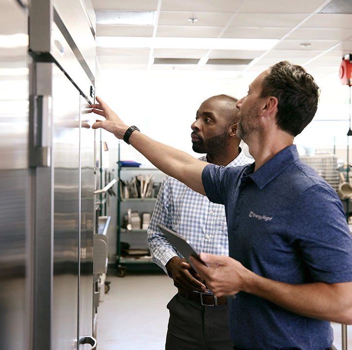 TVA Energy Expert consulting with a customer about energy-efficient commercial refrigeration, pointing at the unit.