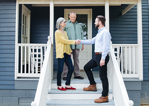 A TVA Energy Expert greets an older couple on their porch, ready to discuss energy-efficient home solutions.