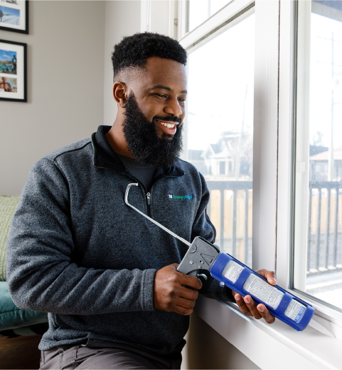 A smiling TVA Energy Expert applies caulk around a window frame, sealing air leaks for improved home energy efficiency.