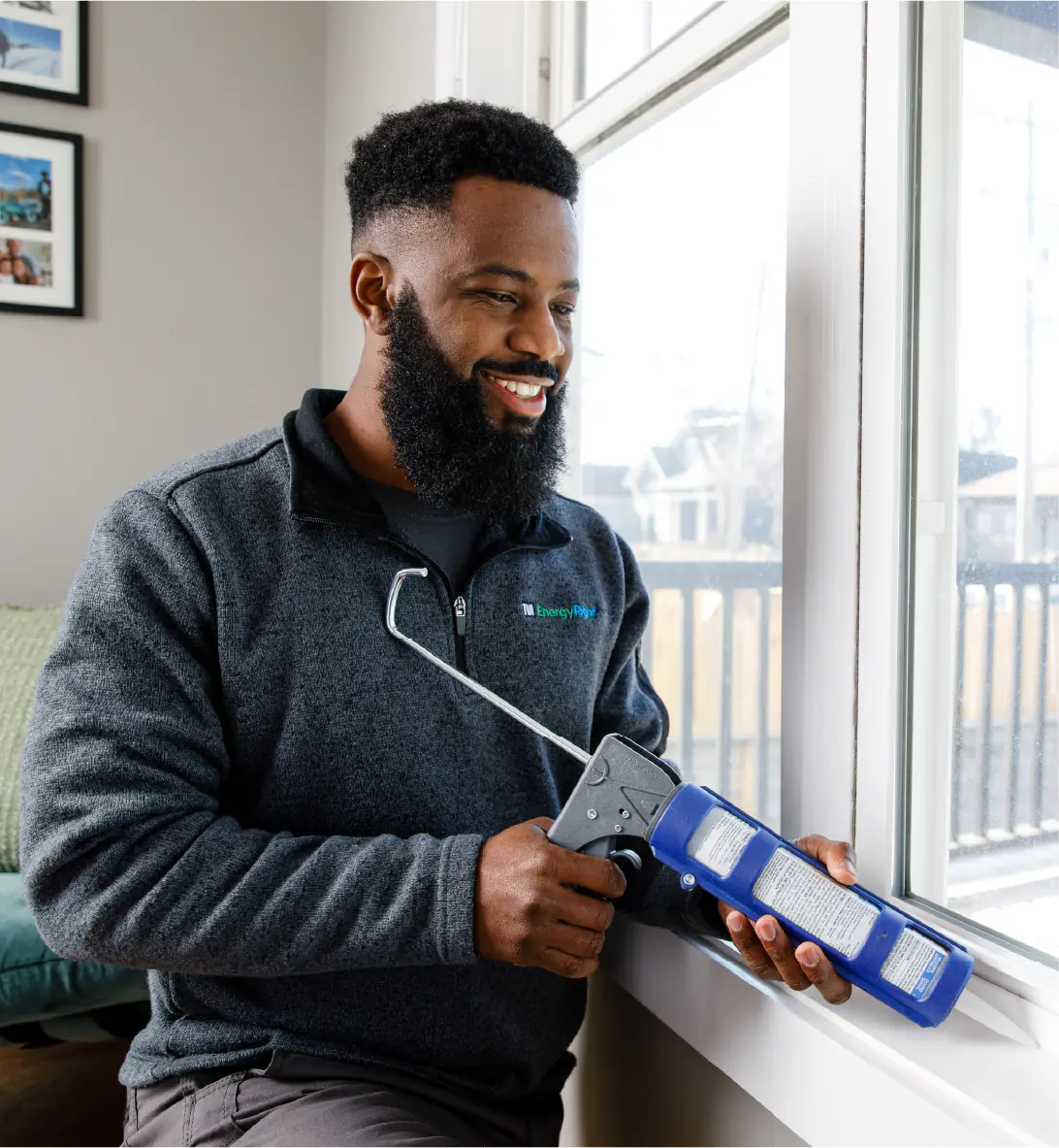 A smiling TVA Energy Expert applies caulk around a window frame, sealing air leaks for improved home energy efficiency.