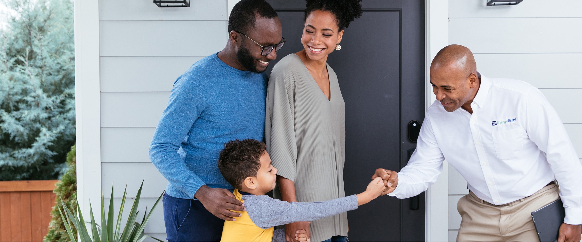 TVA Energy Expert fist-bumps a child as parents smile at their home's front door, highlighting community energy solutions.
