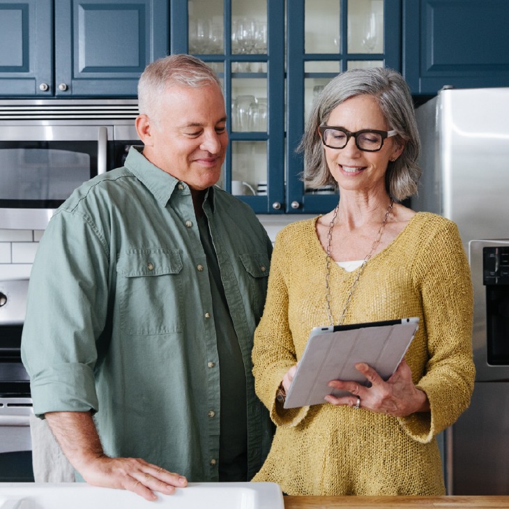 Smiling couple reviews home energy efficiency solutions on a tablet in their modern kitchen, using EnergyRight tools.