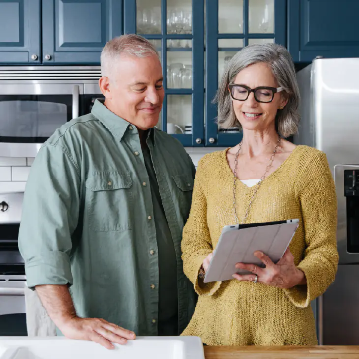 Homeowners review smart thermostat options and energy usage data on a tablet in their modern kitchen.