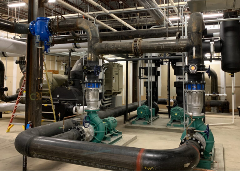 Large commercial HVAC system with intricate piping, multiple green circulation pumps, and a central chiller, showcasing energy efficiency.