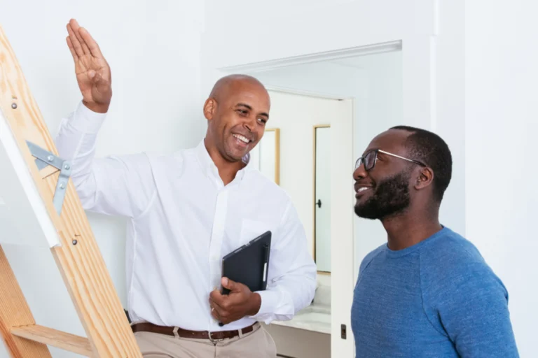 Man pointing toward an attic ladder while talking with another man.