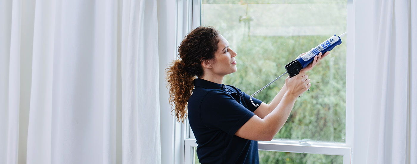 Woman applies sealant around a window.